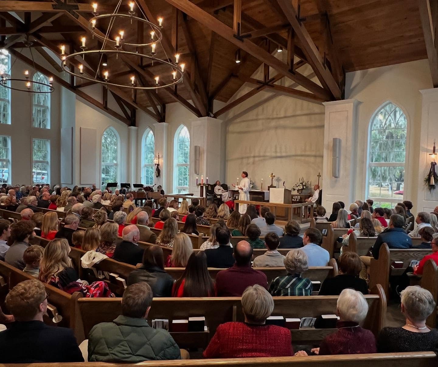 A full sanctuary during Advent worship, beneath a candle chandelier and a timber ceiling