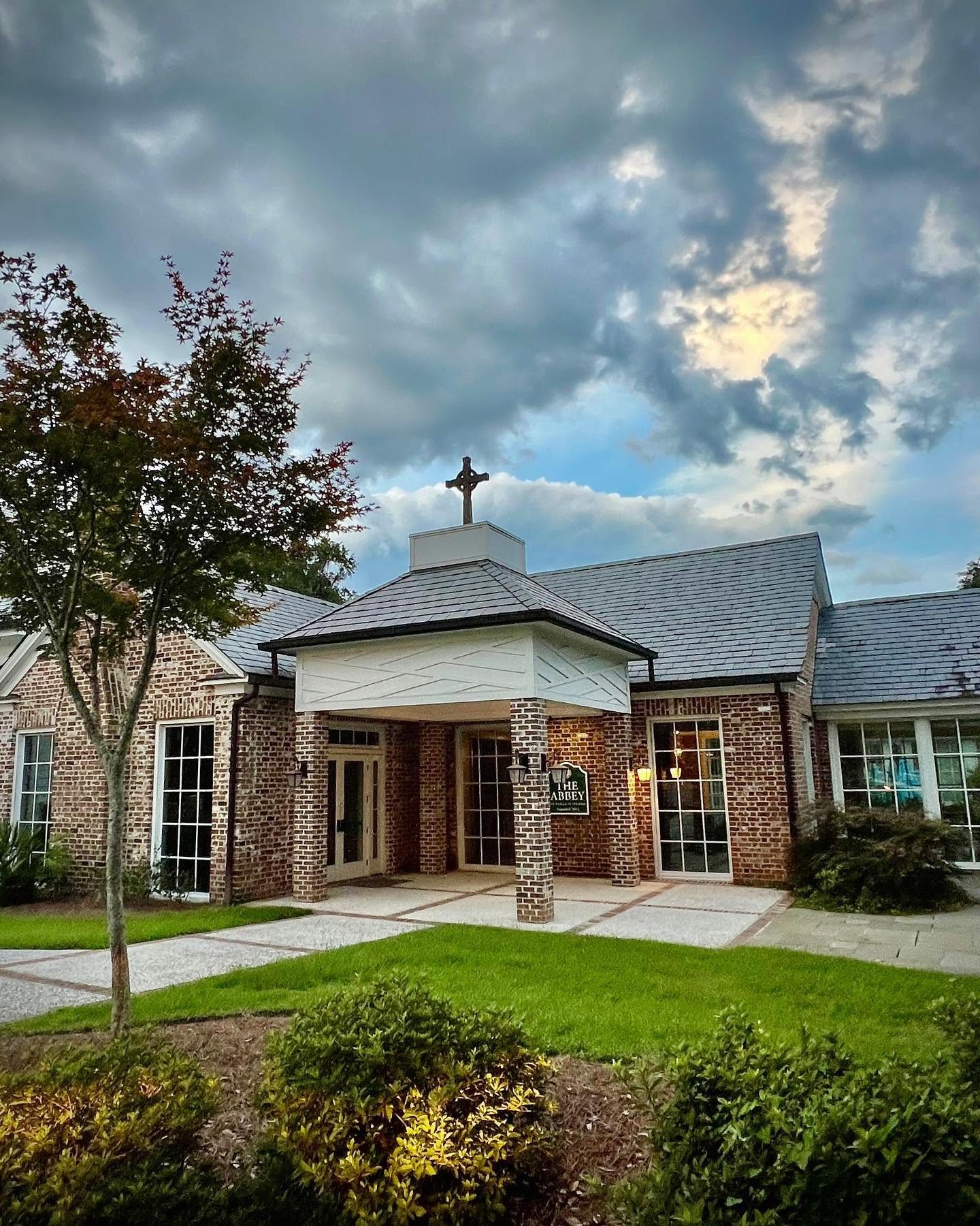 The Abbey’s brick church building, with a Celtic cross atop the cupola, under a dramatic evening sky