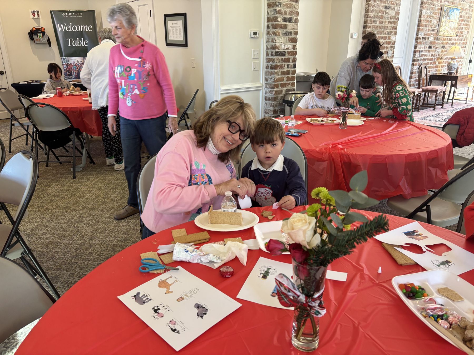 A volunteer and a young boy building a graham cracker gingerbread house at the Gingerbread Bash