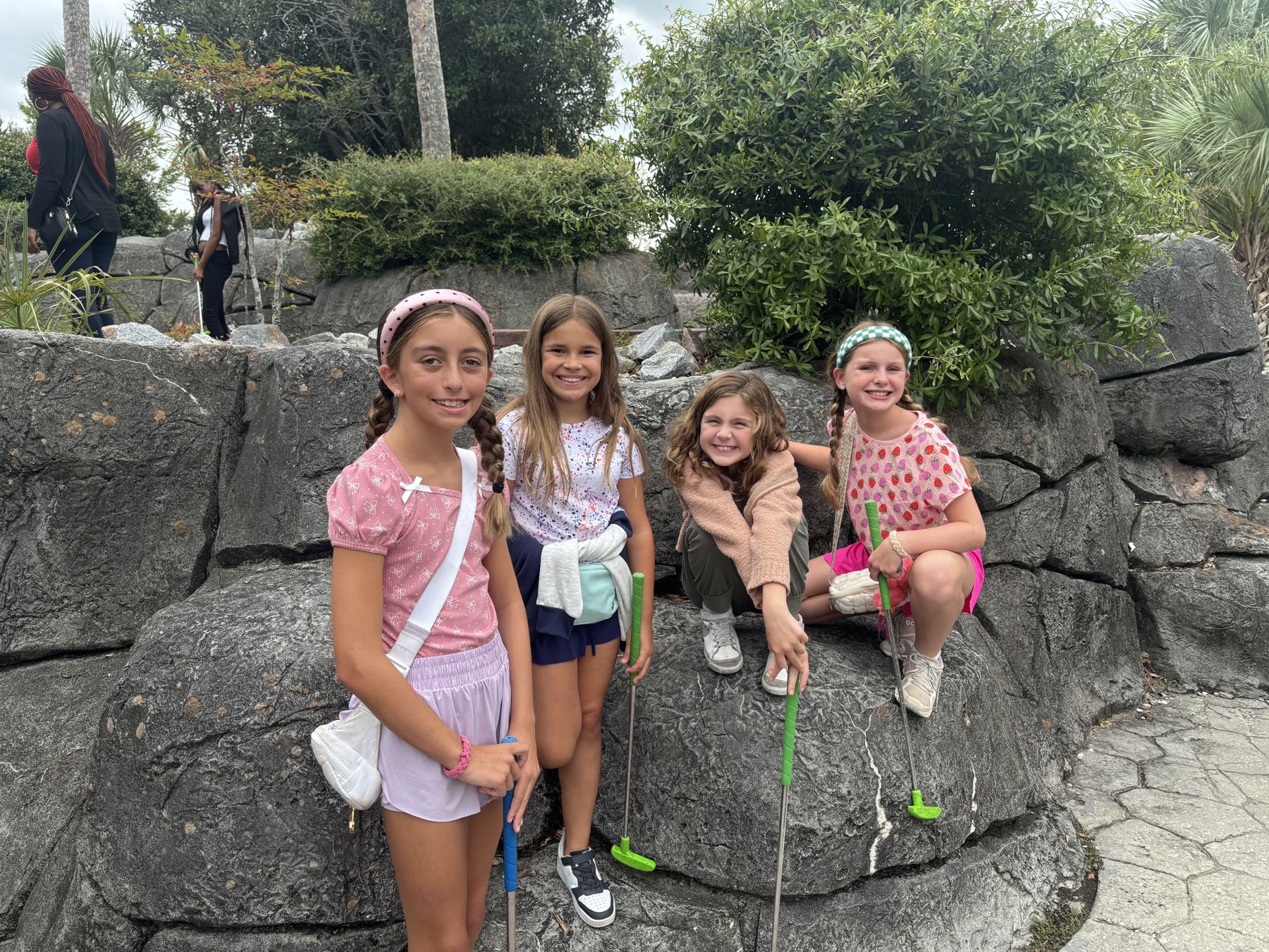 Four smiling girls with putters on the rocks of a mini golf course