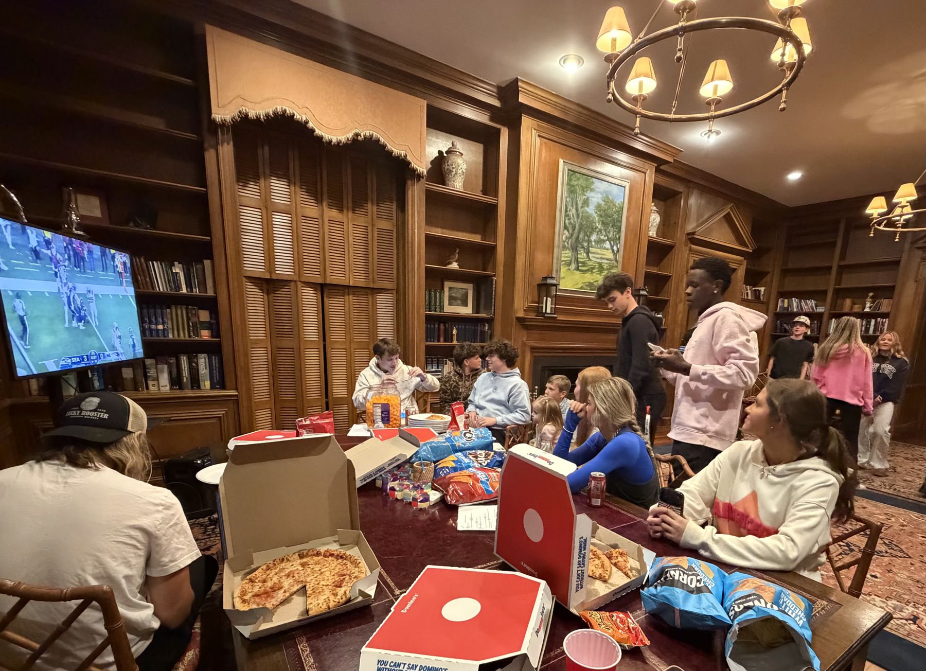 Students sharing pizza and watching football together in a wood-paneled library